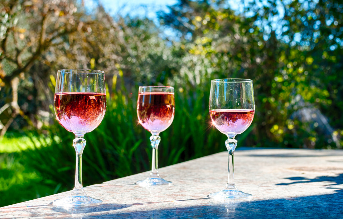Tre calici di vino rosato su un tavolo all'aperto in un giardino con ulivi
